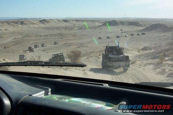 Desert convoy with modified off-road vehicles, viewed from inside a car