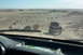 1995 Ford Bronco - A group of off-road vehicles traverses a sandy desert terrain under a clear sky.