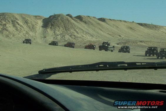 Several off-road vehicles driving on sand dunes under a clear blue sky
