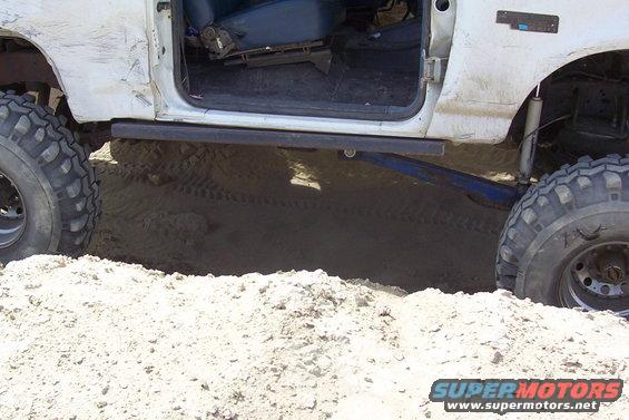White off-road vehicle with large tires partially submerged in sand, showing the open driver's side door and interior