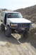 1995 Ford Bronco - A white Ford Bronco navigates a sandy terrain, with other vehicles and people visible in the background.