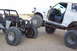 1995 Ford Bronco - Two modified off-road vehicles are positioned closely together on a dirt surface under a bright sky.