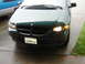 1997 Dodge Grand Caravan - Front view of a 1997 Dodge Grand Caravan, showing its headlights and grille. A second vehicle is partly visible.