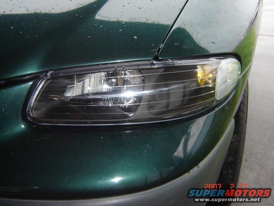 Close-up of a dark green vehicle's headlight assembly. Water droplets on the hood