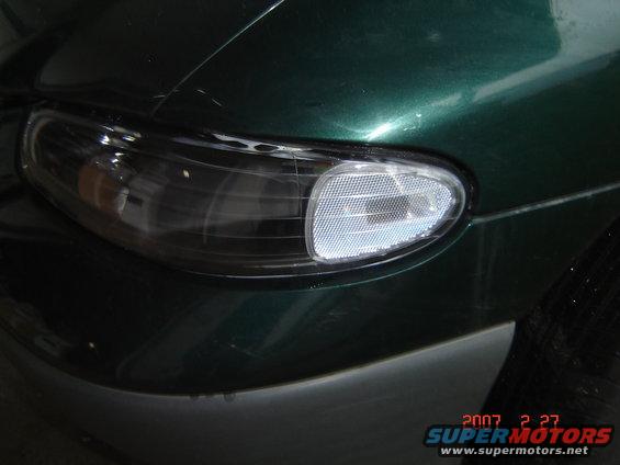 Close-up of a dark-tinted headlight assembly with a clear reflector, mounted on a dark green car body