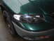 1997 Dodge Grand Caravan - A close-up of a green minivan's front corner, showing the headlight and fender with water droplets.