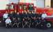 1998 Ford Crown Victoria - A group of firefighters stand and kneel in front of a large red fire truck.