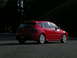 2007 Mazda 3 - A red 2007 Mazda 3 hatchback is parked on asphalt with a dark forest background.
