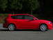 2007 Mazda 3 - A red Mazda 3 hatchback is parked on an asphalt road with trees in the background.