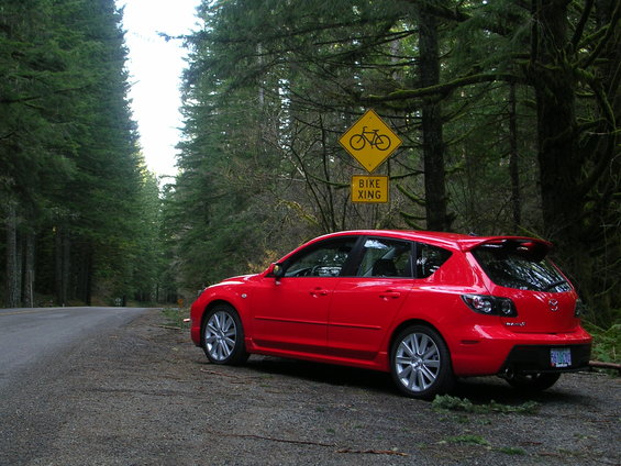 Red 2007 Mazda 3 hatchback parked on forest road with bike crossing sign