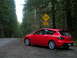 2007 Mazda 3 - A red 2007 Mazda 3 hatchback is parked on the side of a road in a forest, with a "Bike Xing" sign visible.