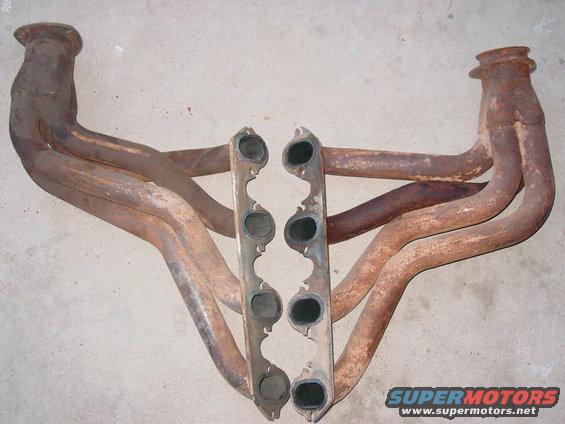 Pair of rusty exhaust manifolds with eight ports, laid out on a concrete surface