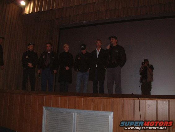 Several people stand on a stage in front of a large screen, with a photographer in the background