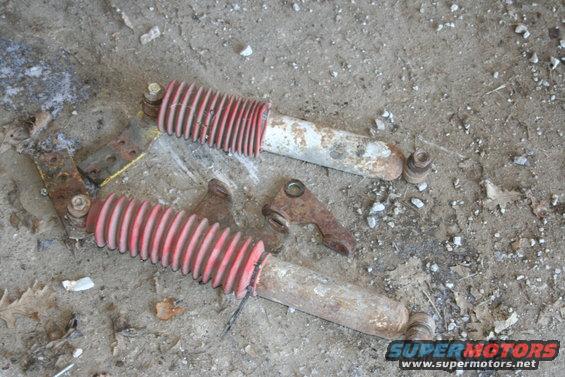 Pair of red and white lift kit shocks with mounting hardware on the ground