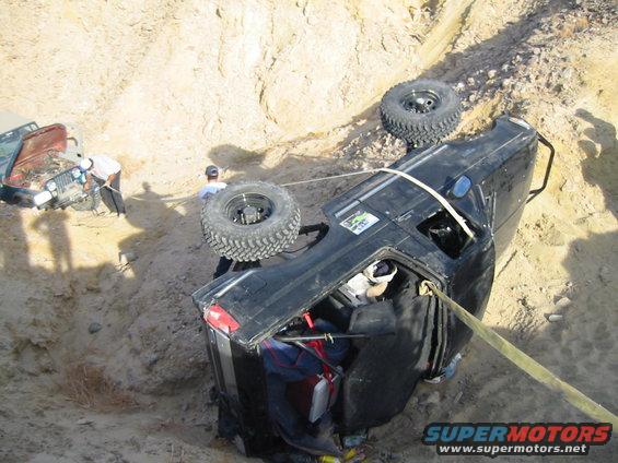 Black 1992 Ford Bronco rolled onto its side, being winched out of a ditch