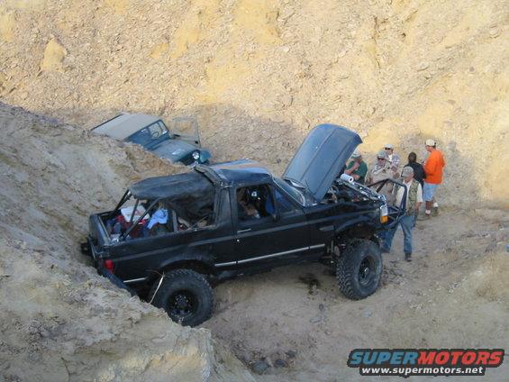 1992 Ford Bronco with open hood stuck in dirt, another vehicle partially visible behind it