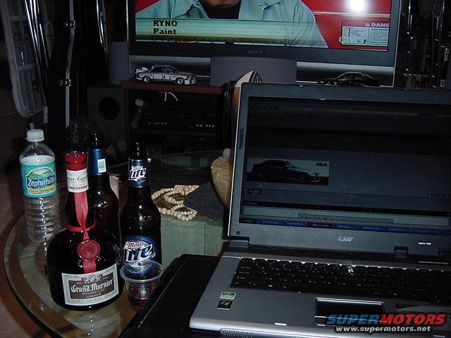Laptop screen shows a dark car, with a television in the background displaying a man and text