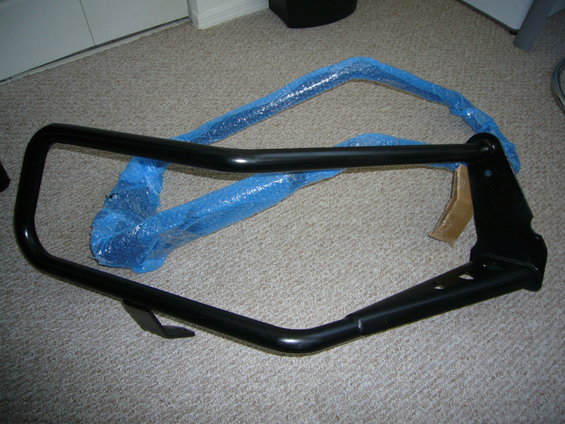Black metal bull bar, partially wrapped in blue bubble wrap, lying on a carpeted floor