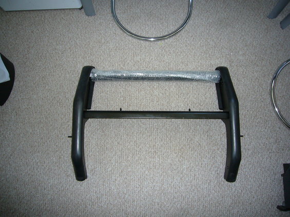 Black bull bar with a clear plastic wrap on the horizontal bar, lying on a carpeted floor