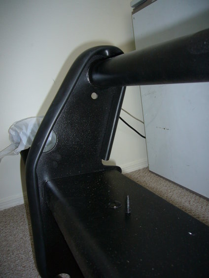 Black plastic bumper component with a horizontal metal bar attached. A screw is visible on the surface