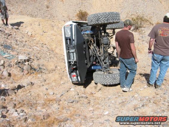 White off-road vehicle overturned on its side, showing suspension and large tires