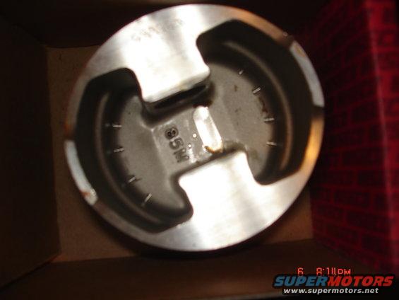 Close-up of a piston with '85M' cast into it, sitting in a box