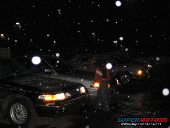 Front view of a black car at night with snow falling