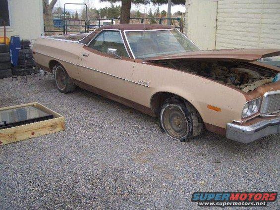Tan 1974 Ford Ranchero with flat front tire and hood open