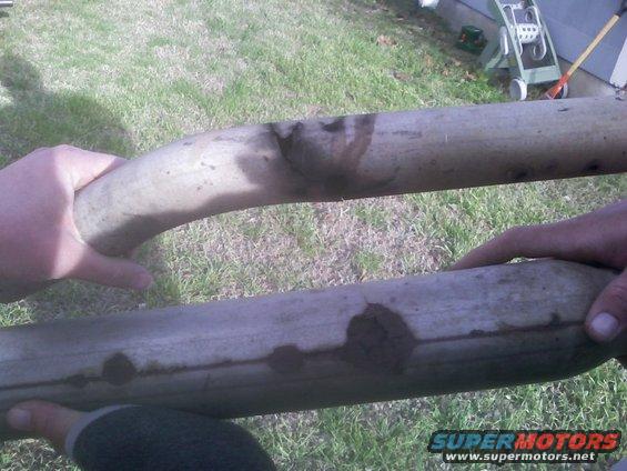 Two exhaust pipes being held by hands, showing some dark staining