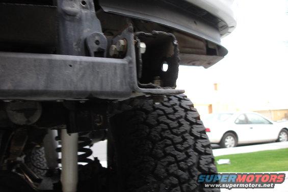 Rear bumper bracket and tire of an off-road vehicle. White car in background