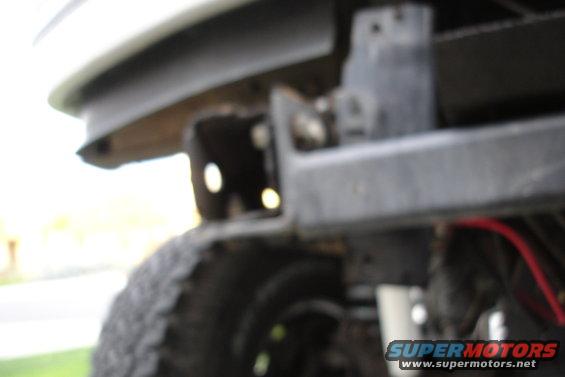 Close-up of a vehicle's bumper mounting bracket with a tire visible below