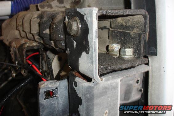 Close-up of a dirty metal bracket with bolts, showing wiring and part of a vehicle frame