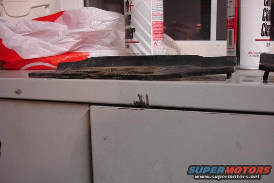 Damaged black rubber trim piece on a workbench with cleaning supplies
