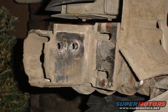 Close-up of a rusty metal bumper bracket with two bolt holes