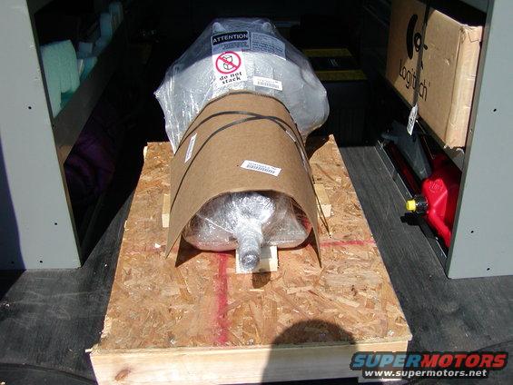 Transmission wrapped in plastic and cardboard on a wooden pallet inside a vehicle. A red gas can and a Logitech box are visible