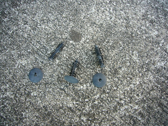 Four black plastic clips and two round washers on a textured concrete surface