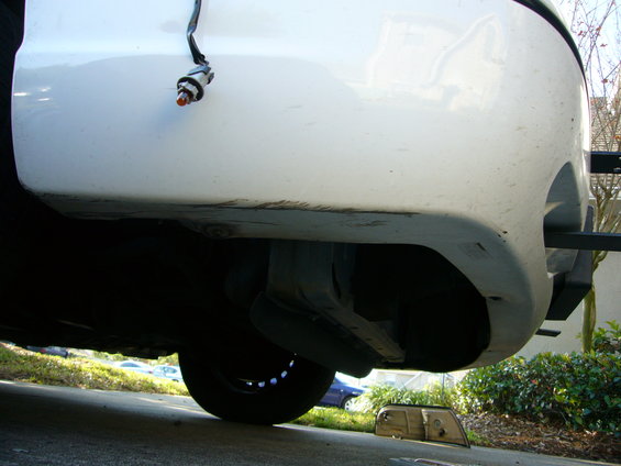 White 2000 Ford Crown Victoria front bumper, viewed from below, showing the undercarriage and a detached headlight
