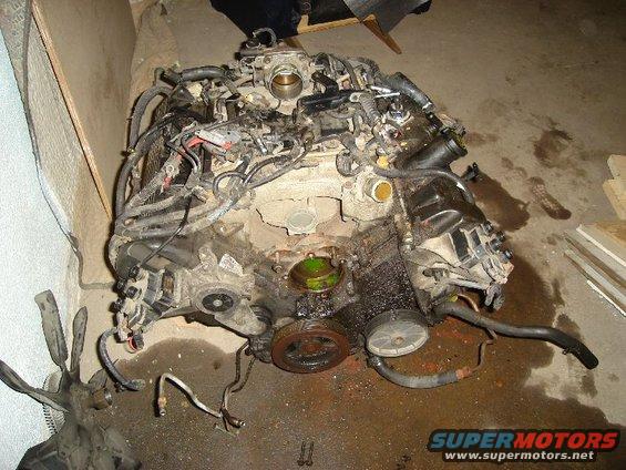 Engine block with hoses and wiring disconnected, sitting on a concrete floor