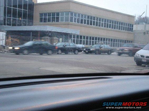 Four cars in a parking lot, including a black sedan and a police car