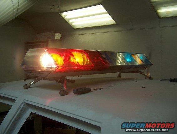 Lightbar with red, amber, and blue lights on top of a car roof. Screwdrivers are on the roof