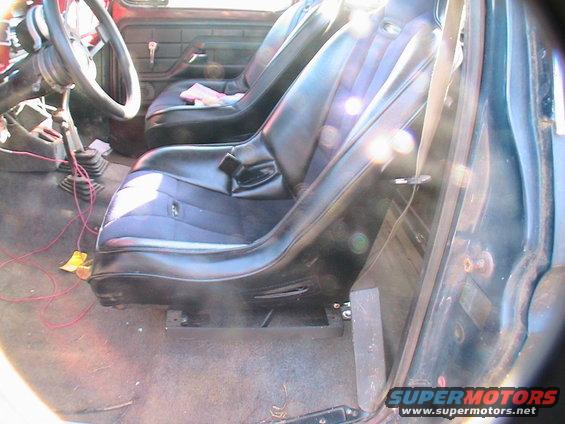 Interior view of a 1977 Ford F-250 with black bucket seats and a manual transmission