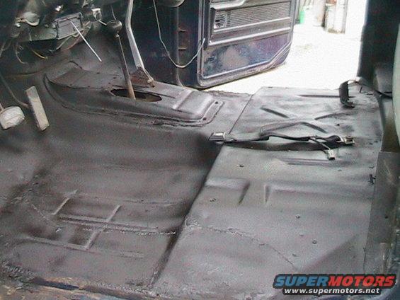Interior floor of a truck, showing the transmission tunnel and seatbelt anchors. The floor appears to have been prepped for coating