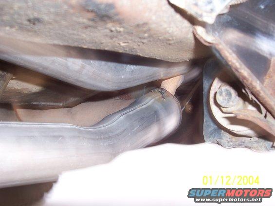 Underside view of vehicle exhaust pipes with visible rust and a Supermotors.net watermark