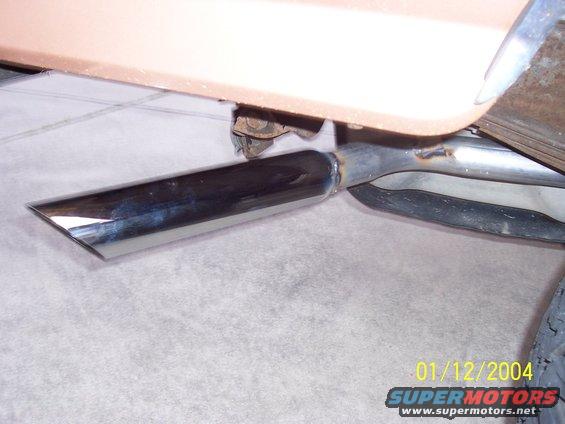 Chrome exhaust tip angled downwards, attached to a tan vehicle body. Welds visible on exhaust pipe