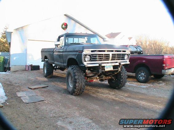 Lifted black 1977 Ford F-250 with large tires parked in front of a garage