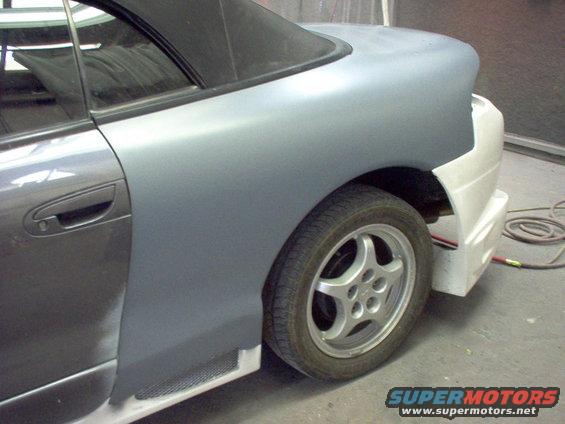 car's rear quarter panel and door in primer, with a black soft top visible