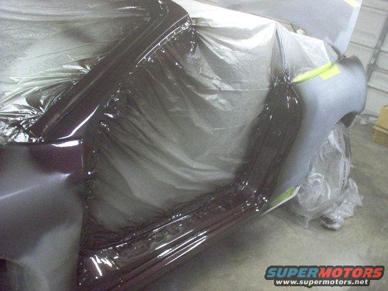 Dark red car body panel covered in plastic sheeting, with gray primer on fender