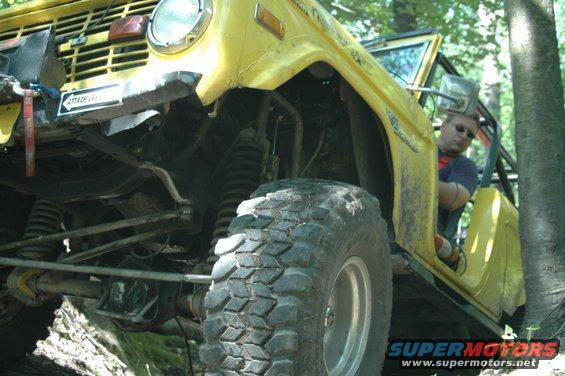 Yellow SUV with large tires on a trail, driver visible inside