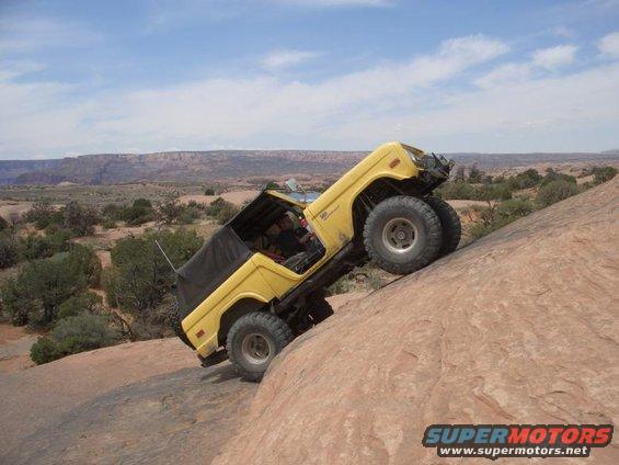 Yellow off-road vehicle with a black soft top climbing a steep rock face
