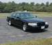 2001 Ford Crown Victoria - A black 2001 Ford Crown Victoria is parked on an asphalt lot with trees in the background.